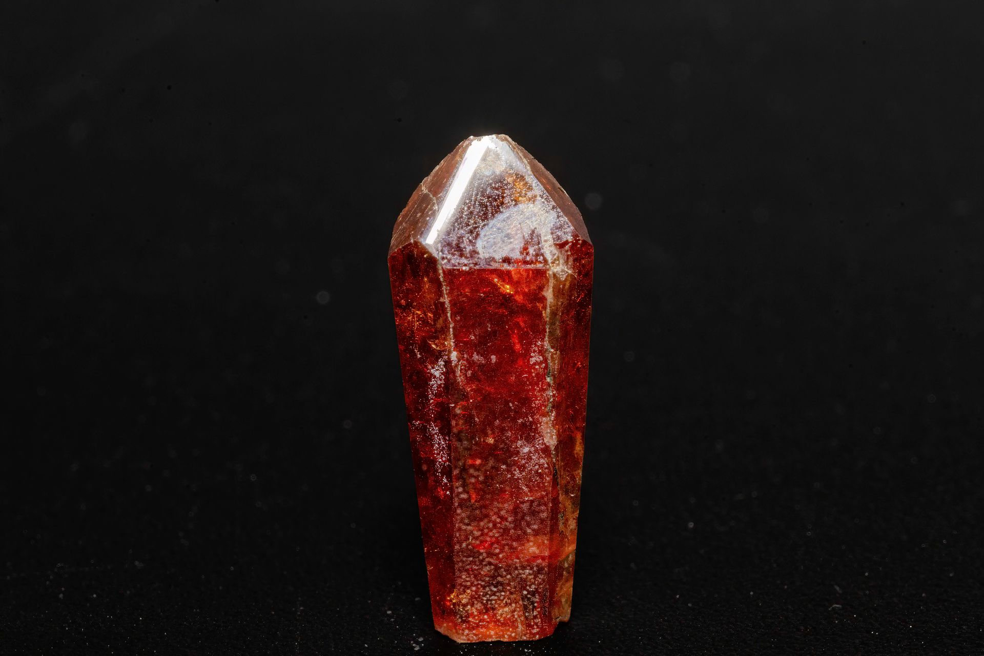 Reddish-brown crystal, elongated with a pointed top, against a dark background.