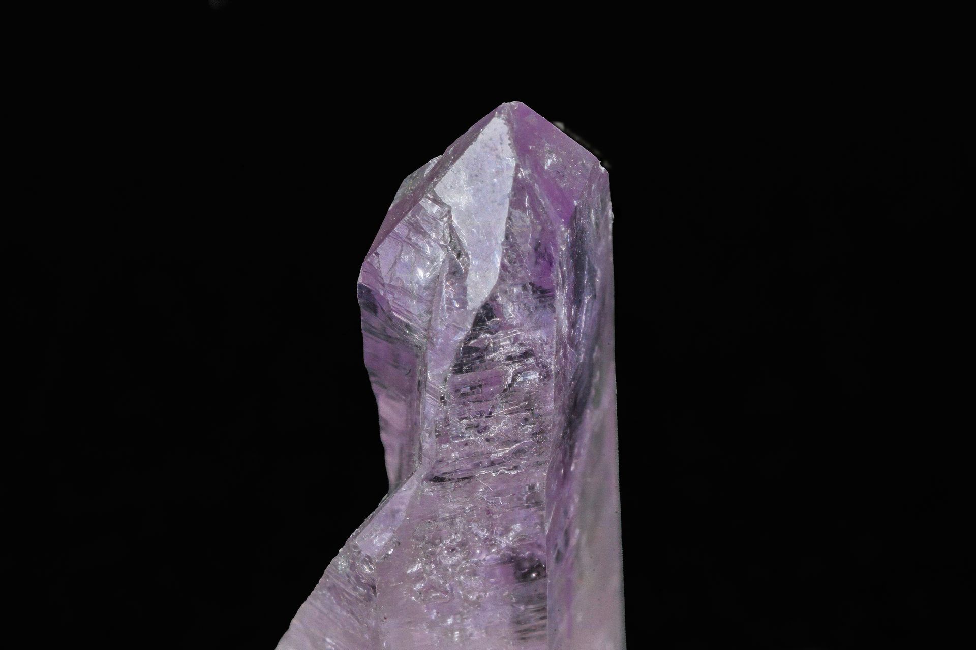 Purple amethyst crystal with a sharp point, against a black background.