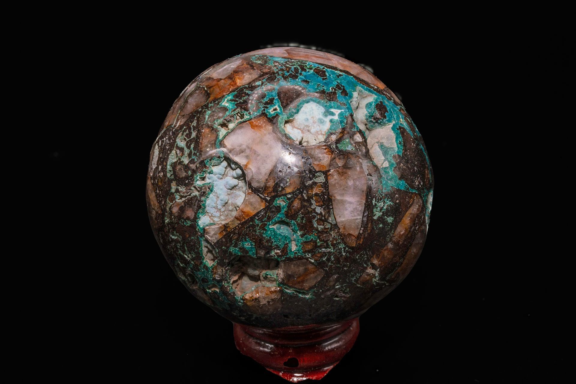 A weathered, multicolored crystal sphere on a red stand against a black background.