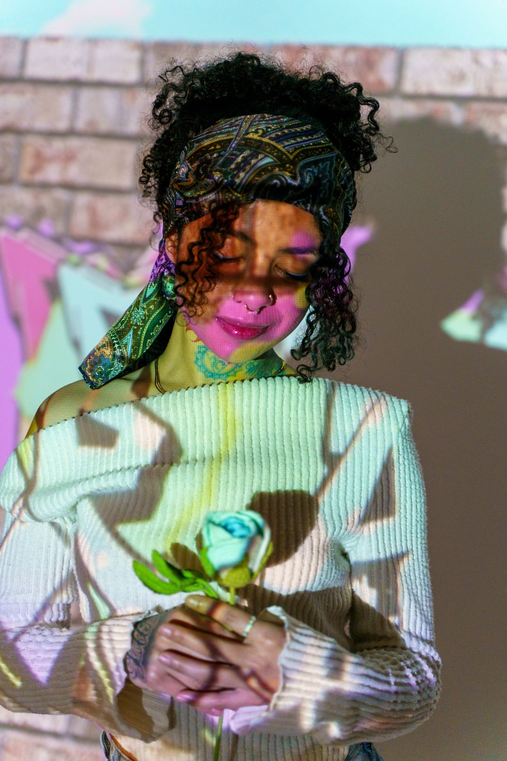 Woman with curly hair holds a blue rose, light projections on her face and clothes.