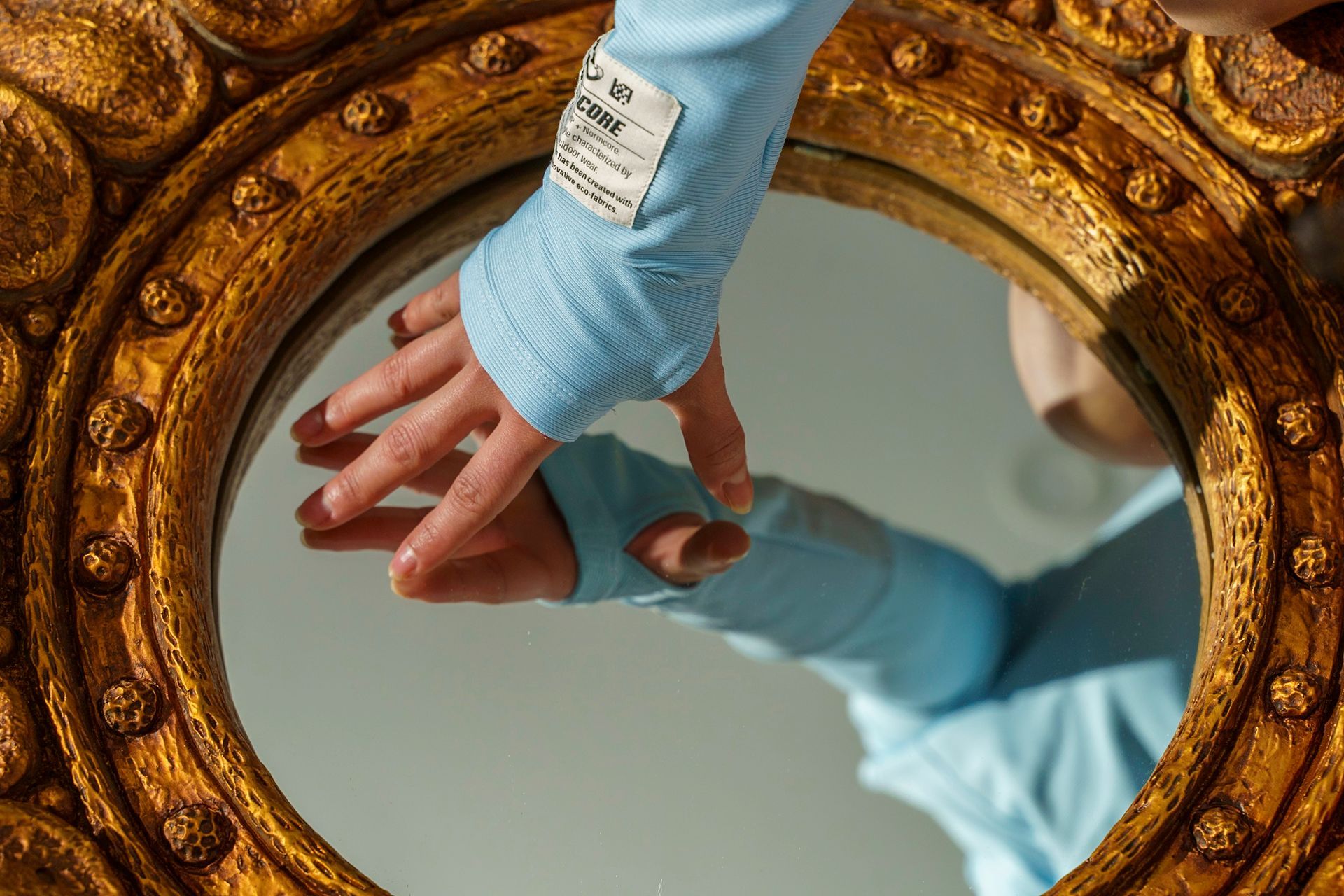 A hand in a blue sleeve reaches into a gold-framed mirror.