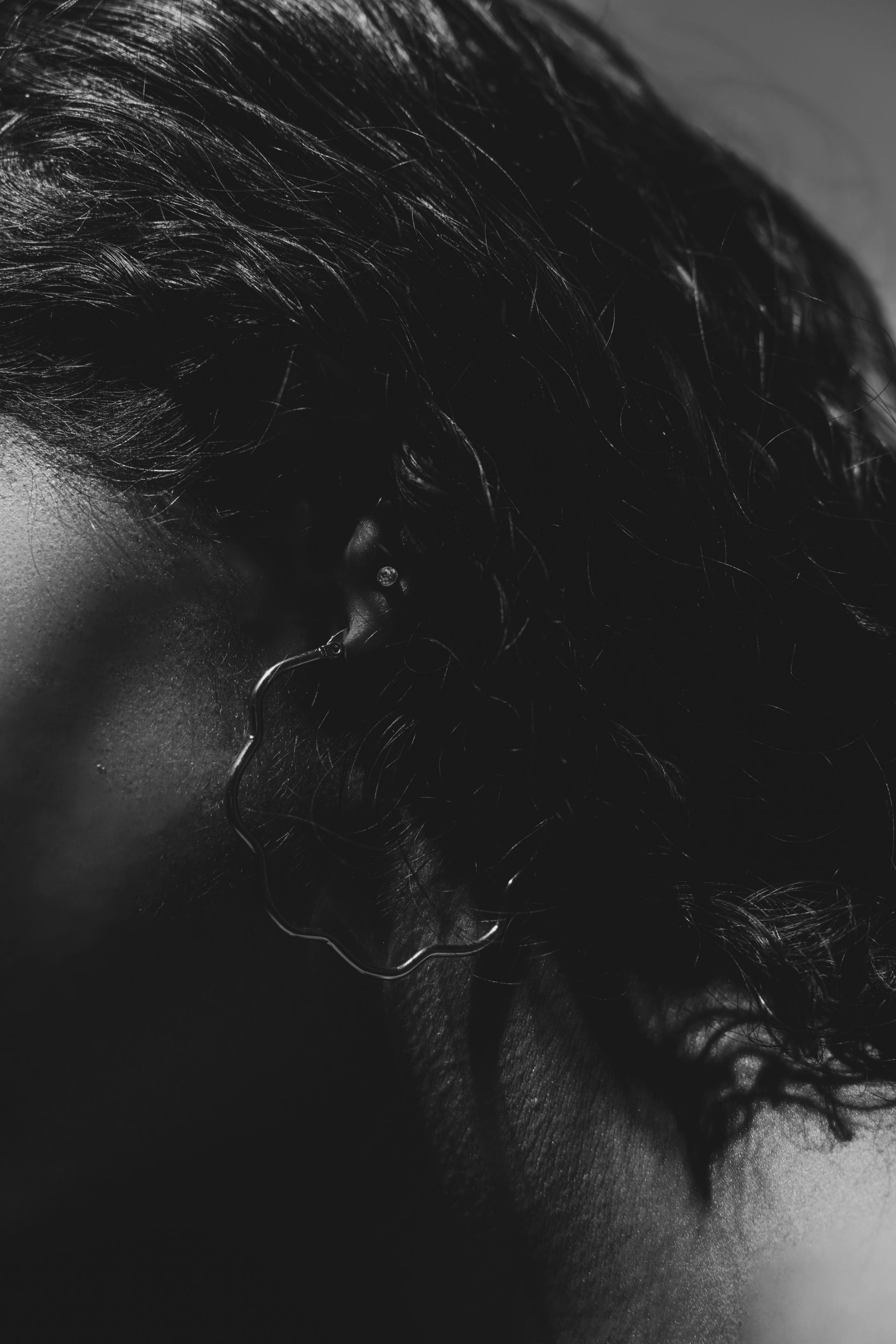 A close-up, black-and-white profile view of a person with curly dark hair and a hoop earring, lit by dramatic side lighting.