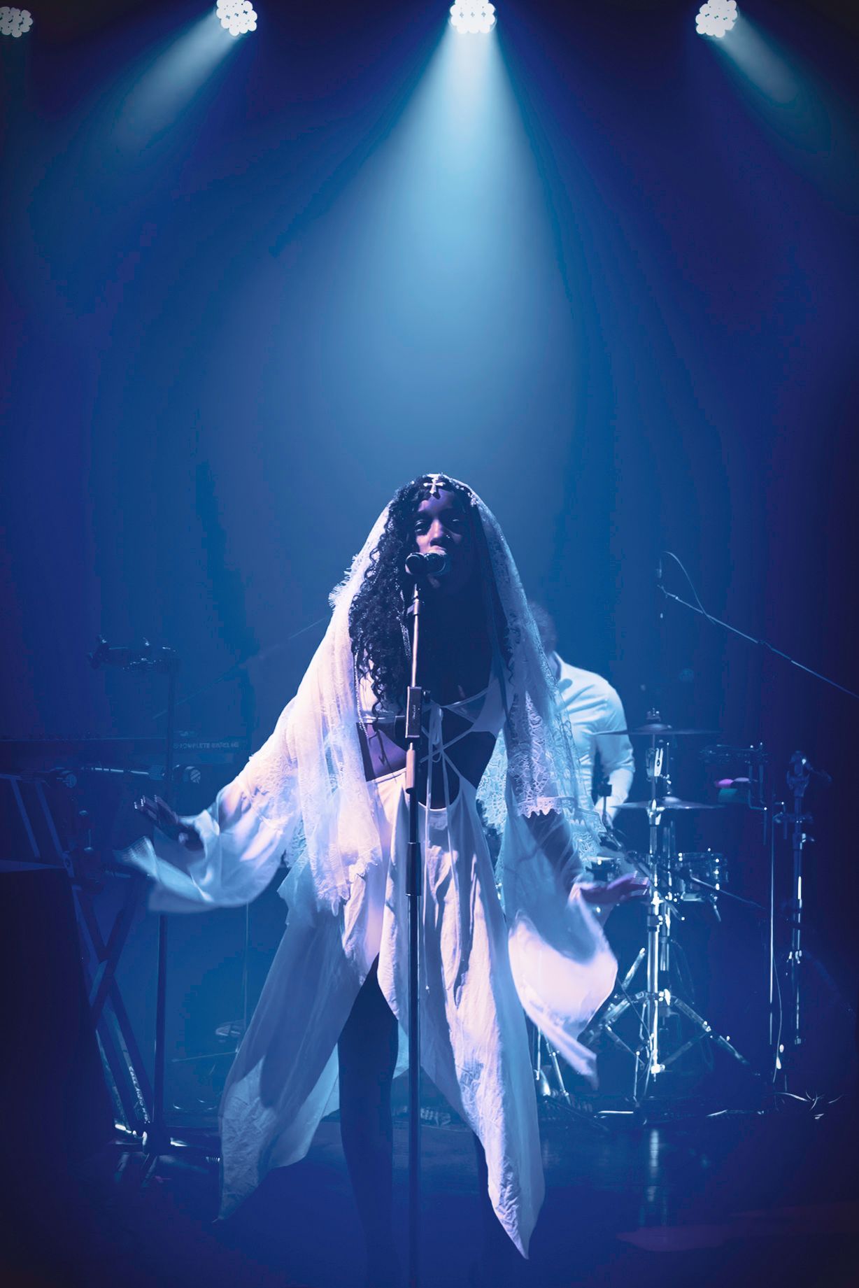 Person in white, flowing outfit performs on stage under blue spotlight.