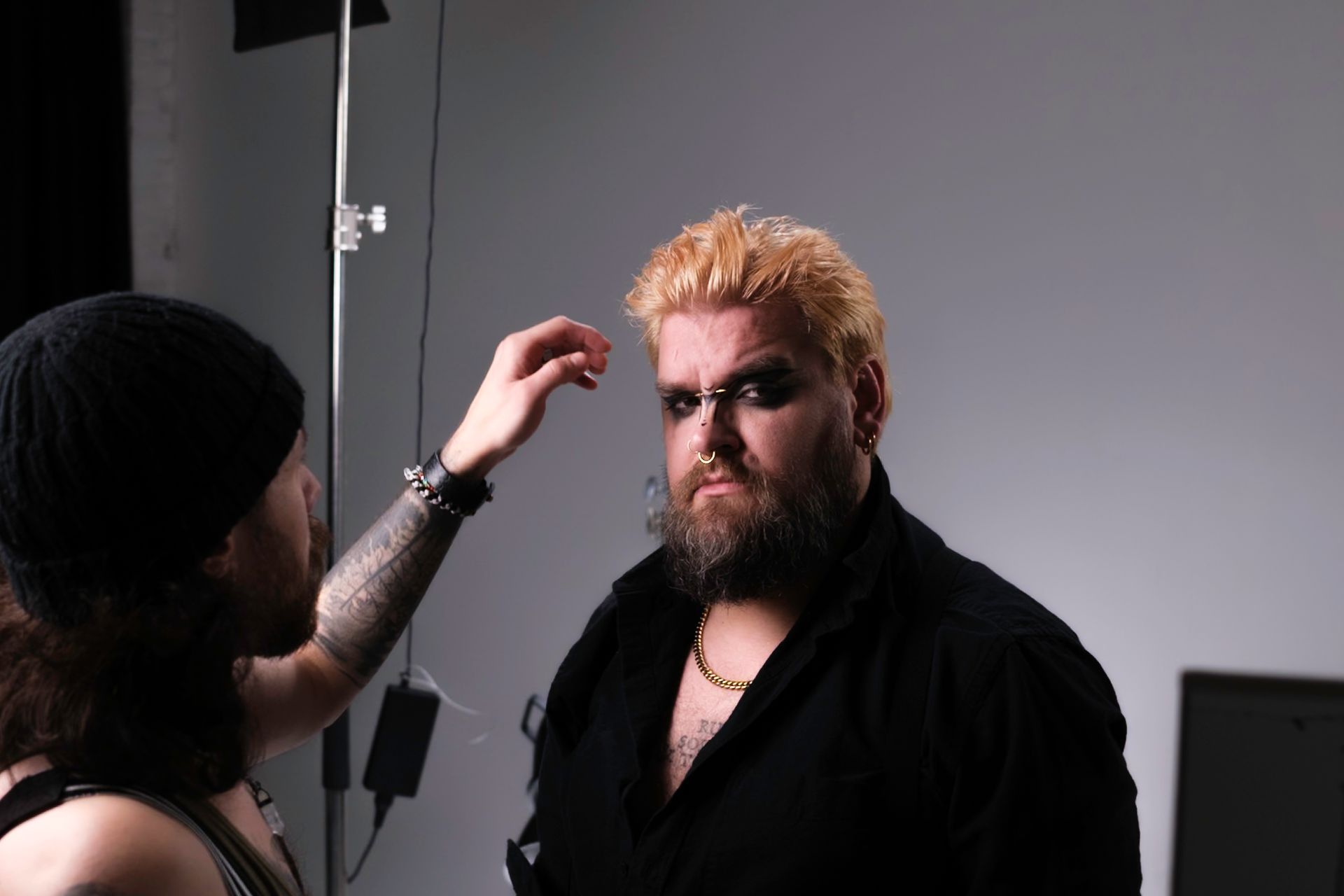 Person with makeup being touched up, studio setting. Black shirt, blonde hair, dark eyeshadow.
