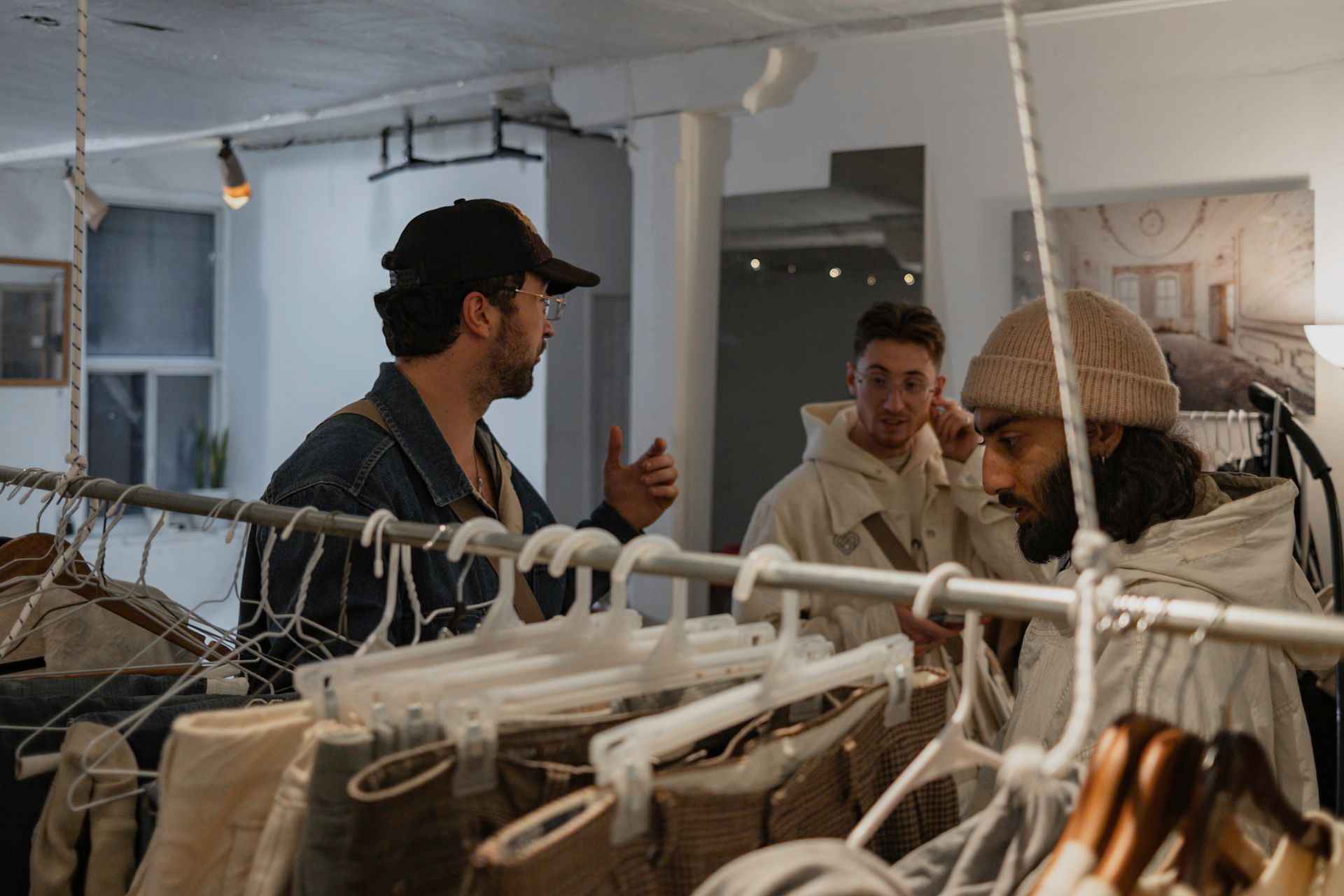 Three people in a clothing store, examining garments on racks. One gestures while others look at clothing.