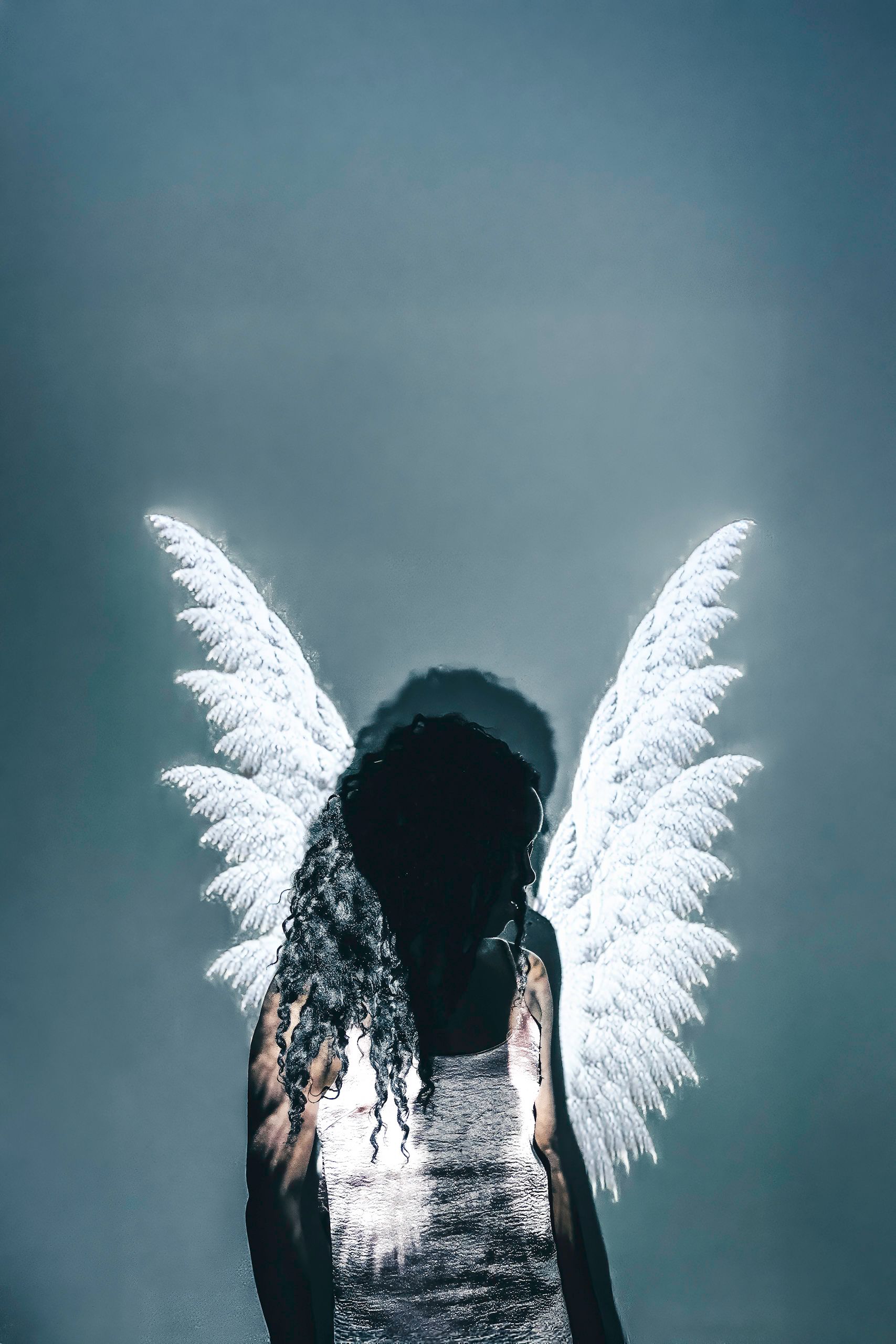 Person with glowing white wings and halo against a blue-gray background.
