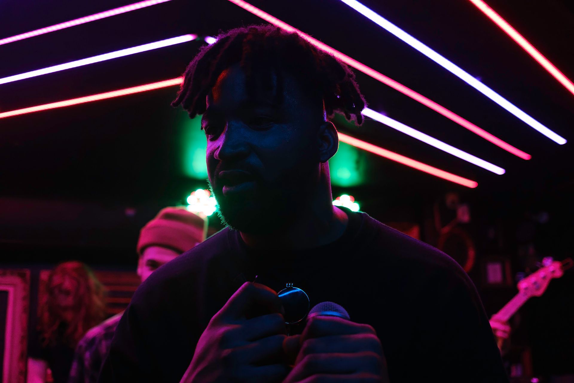 Man singing into microphone on stage, lit by neon lights.