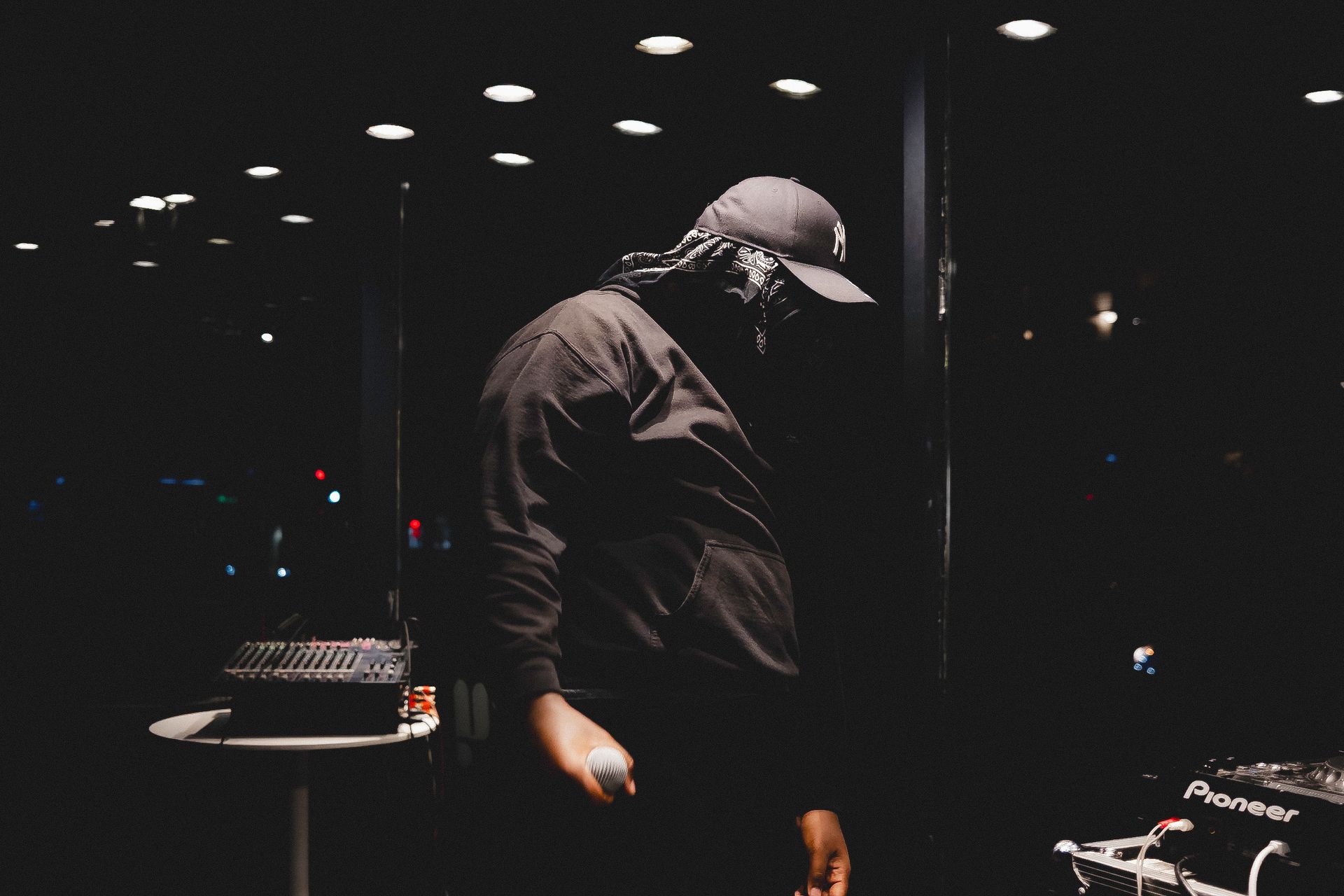 Man wearing a baseball cap and dark clothing, holding a microphone, performing at night.