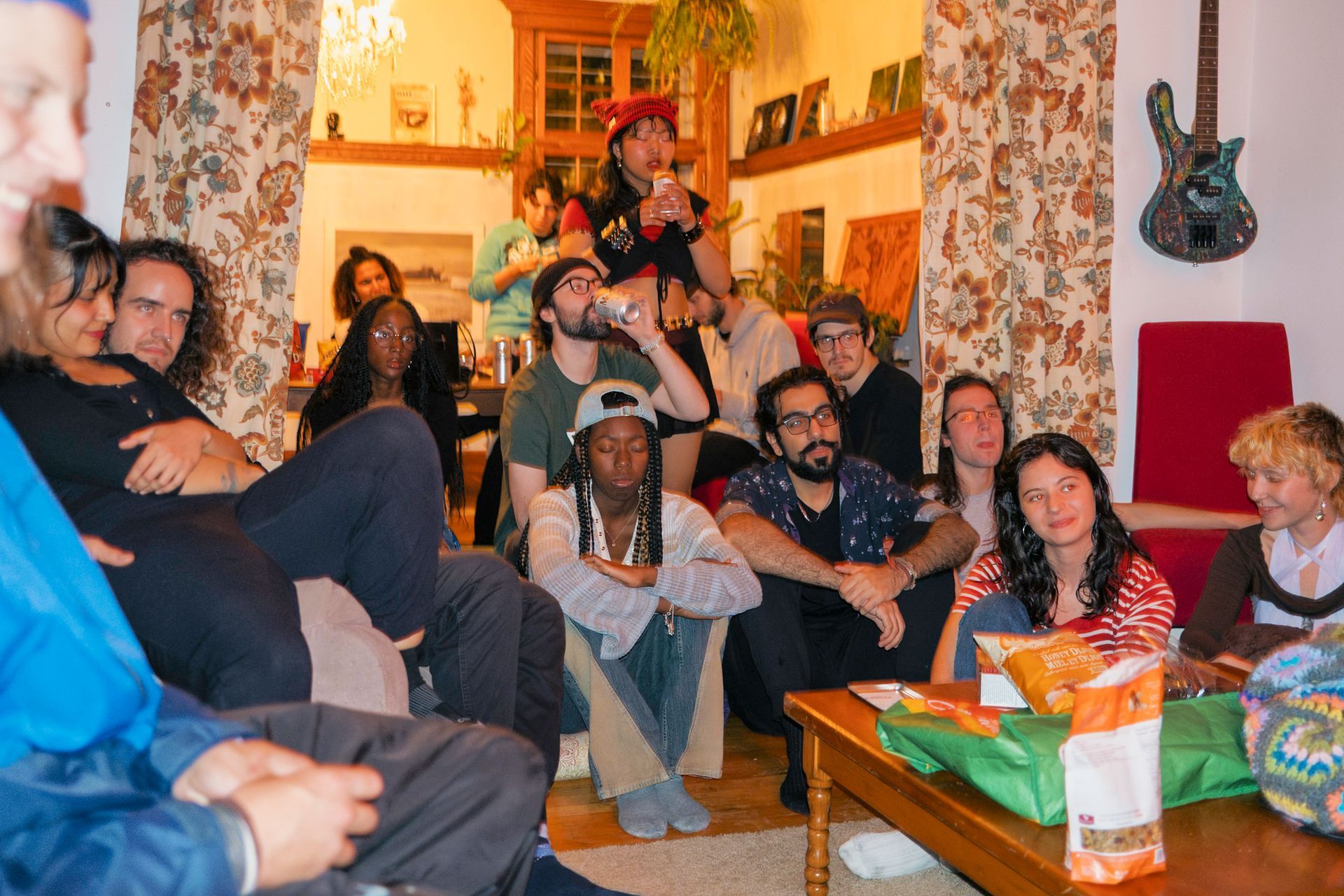 A group of people are gathered indoors, some seated and some standing. They are looking towards the foreground.