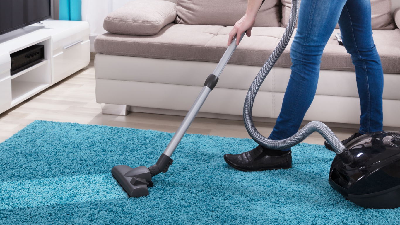 Person wearing pink gloves sprays cleaner and vacuums a carpet.