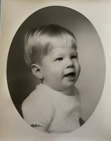 Smiling baby with blonde hair in a studio portrait.