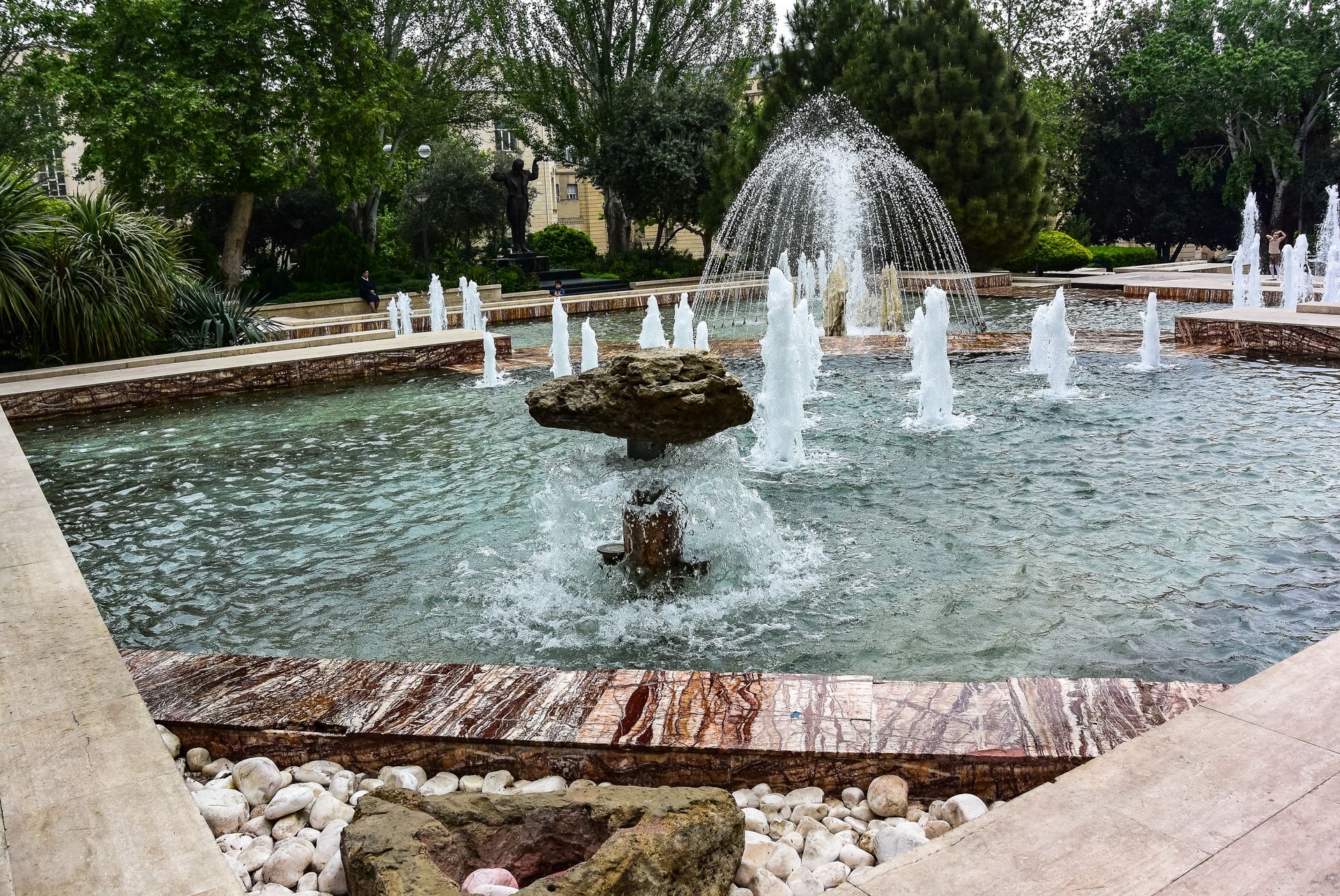 A rectangular fountain with multiple water jets, surrounded by a stone border and landscaping.