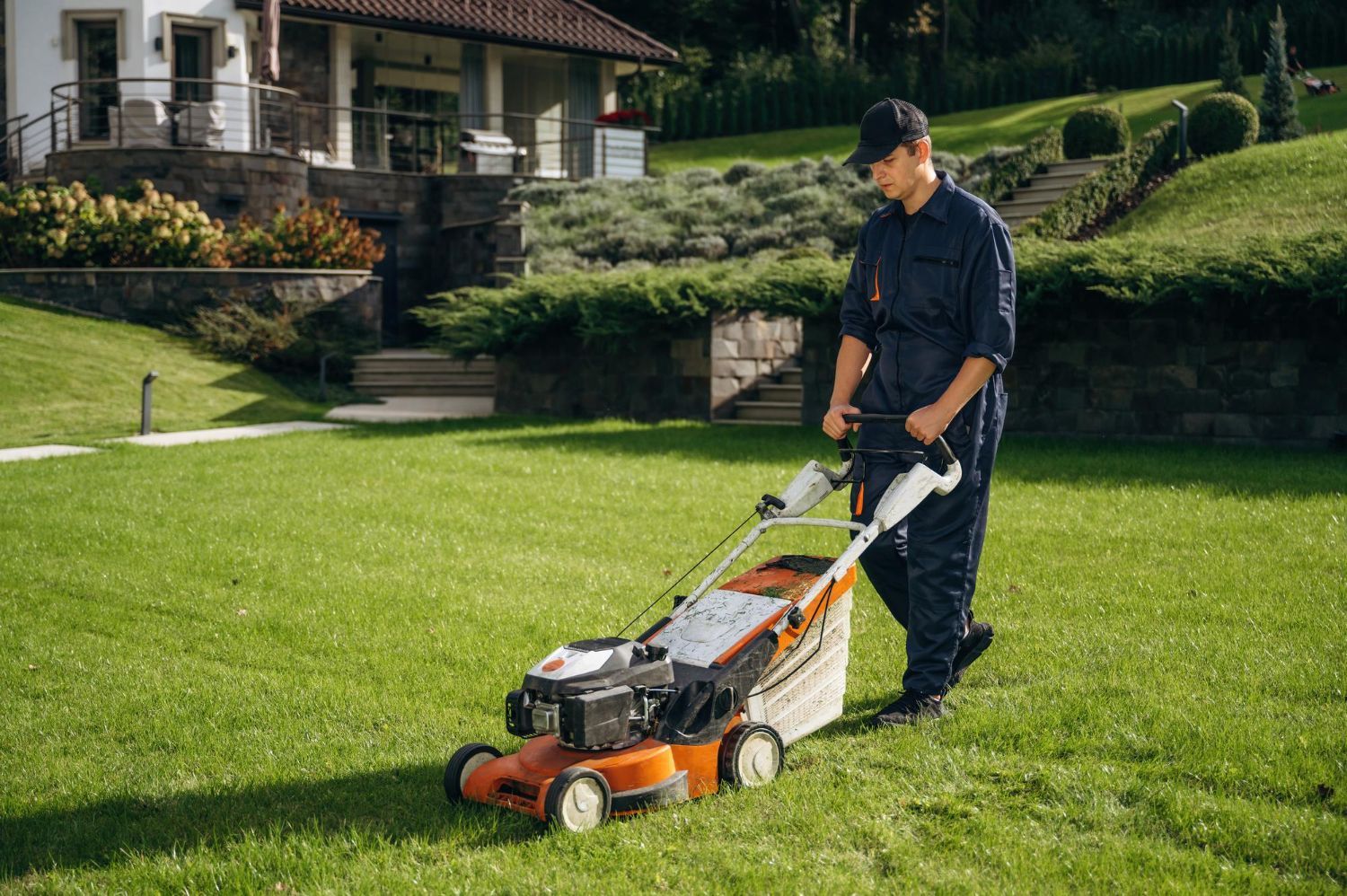 Man mowing a lawn with a push mower in front of a house on a sunny day.