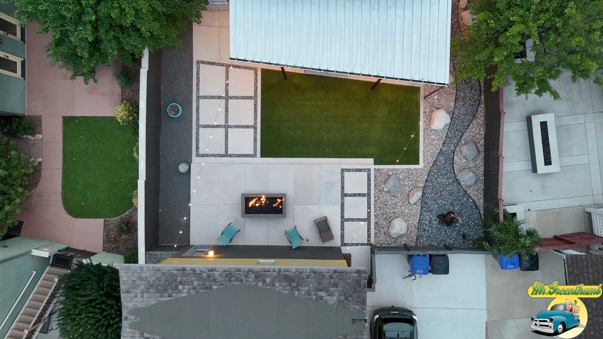 Overhead view of a modern backyard with a fire pit, patio, turf, and a metal pergola roof.