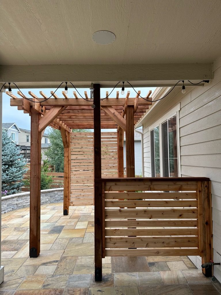 A wooden pergola is attached to the side of a house.