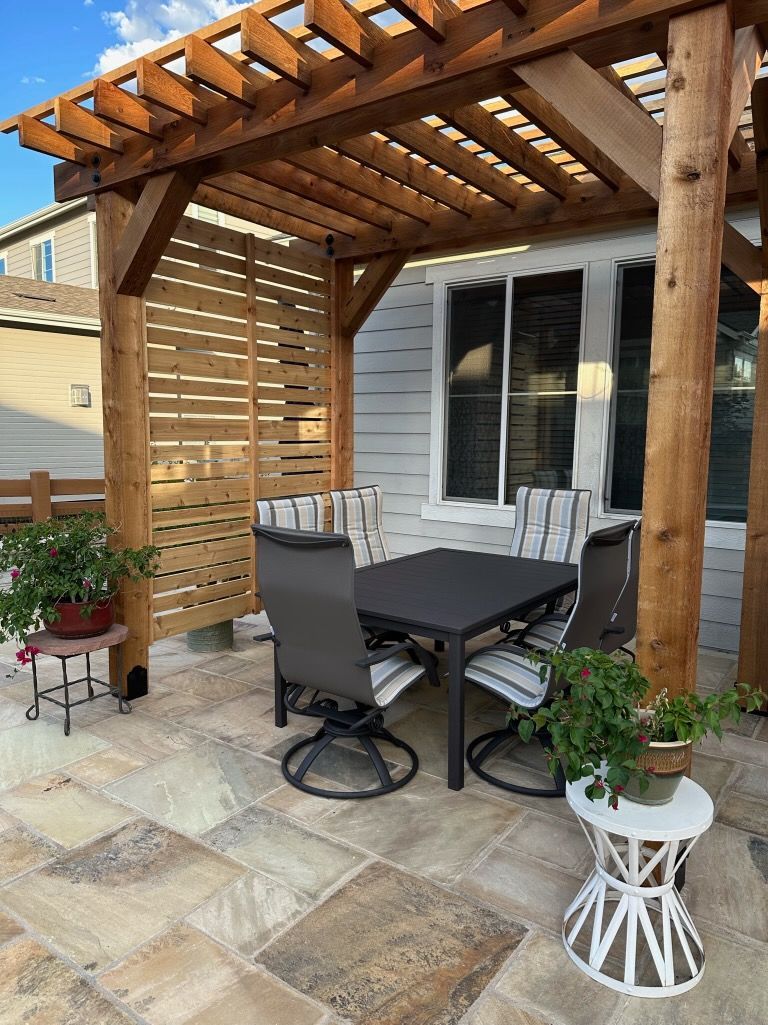 A wooden pergola with a table and chairs underneath it.