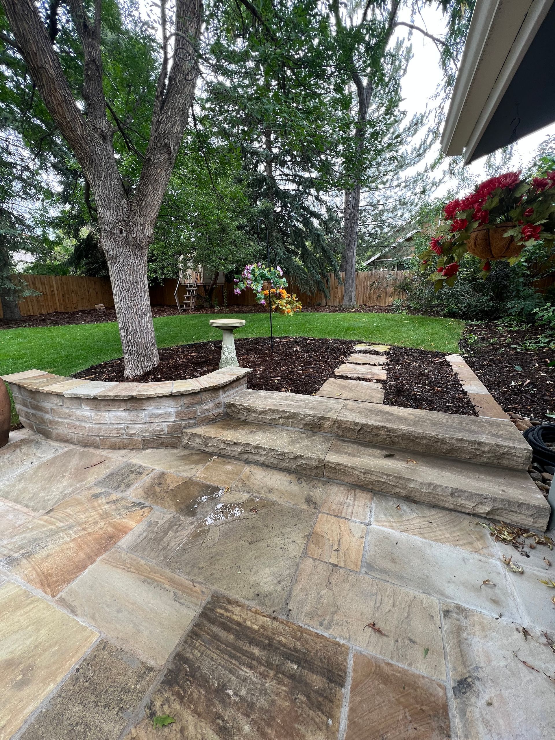 A stone patio with steps leading up to a tree in a backyard.