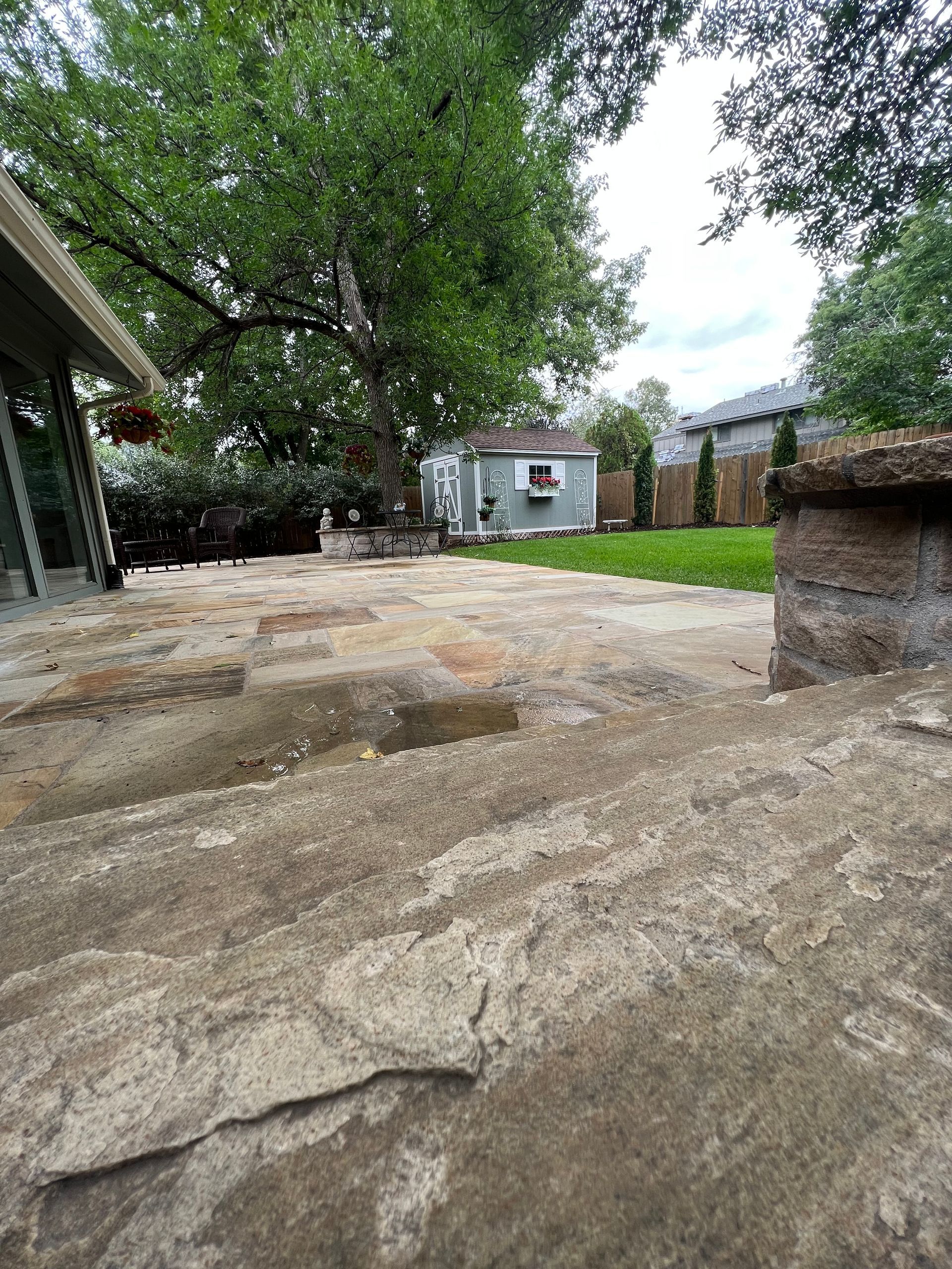 A patio with a shed in the background and trees in the background.