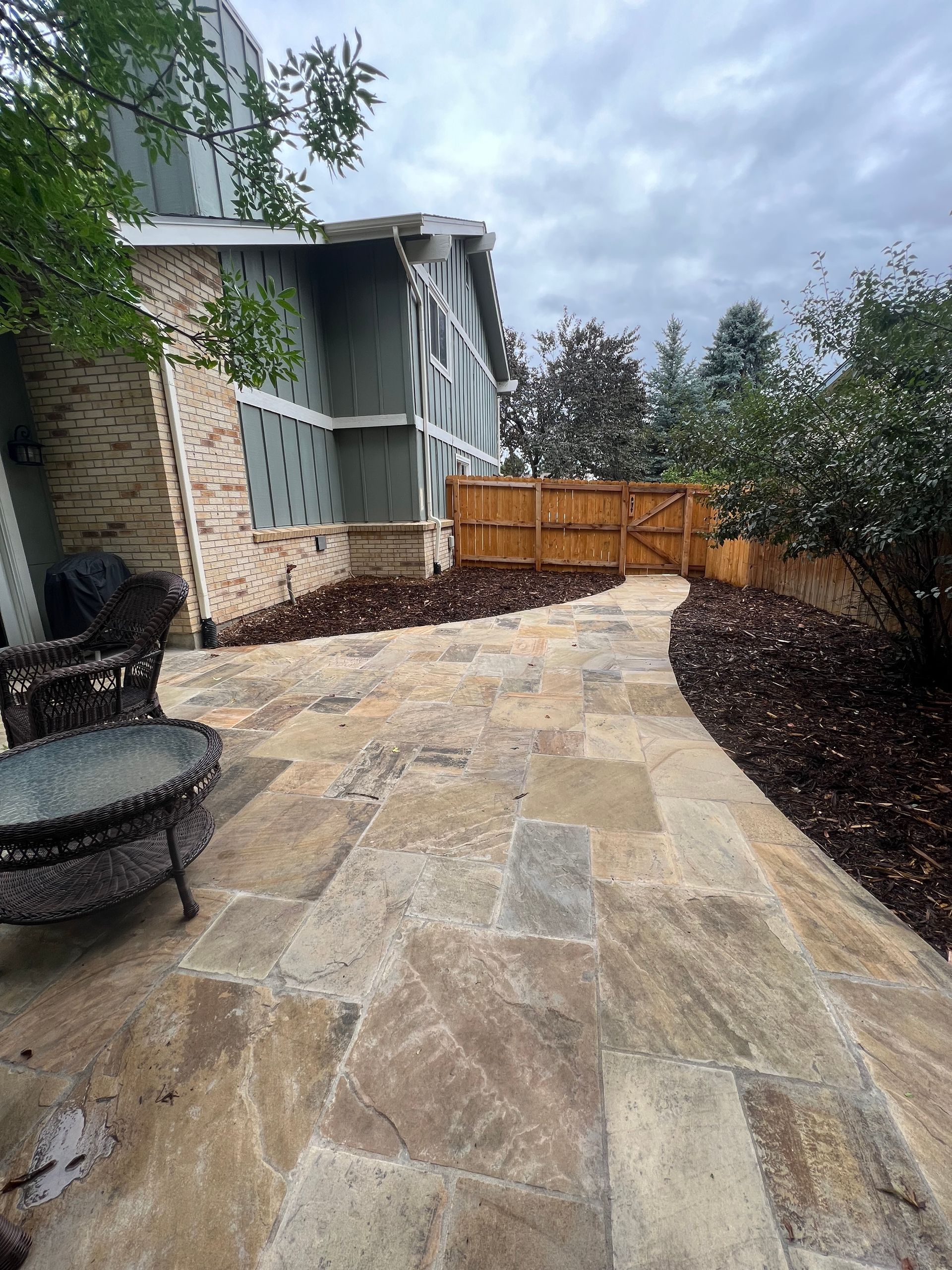 A stone patio with a brick wall and chairs in the background.