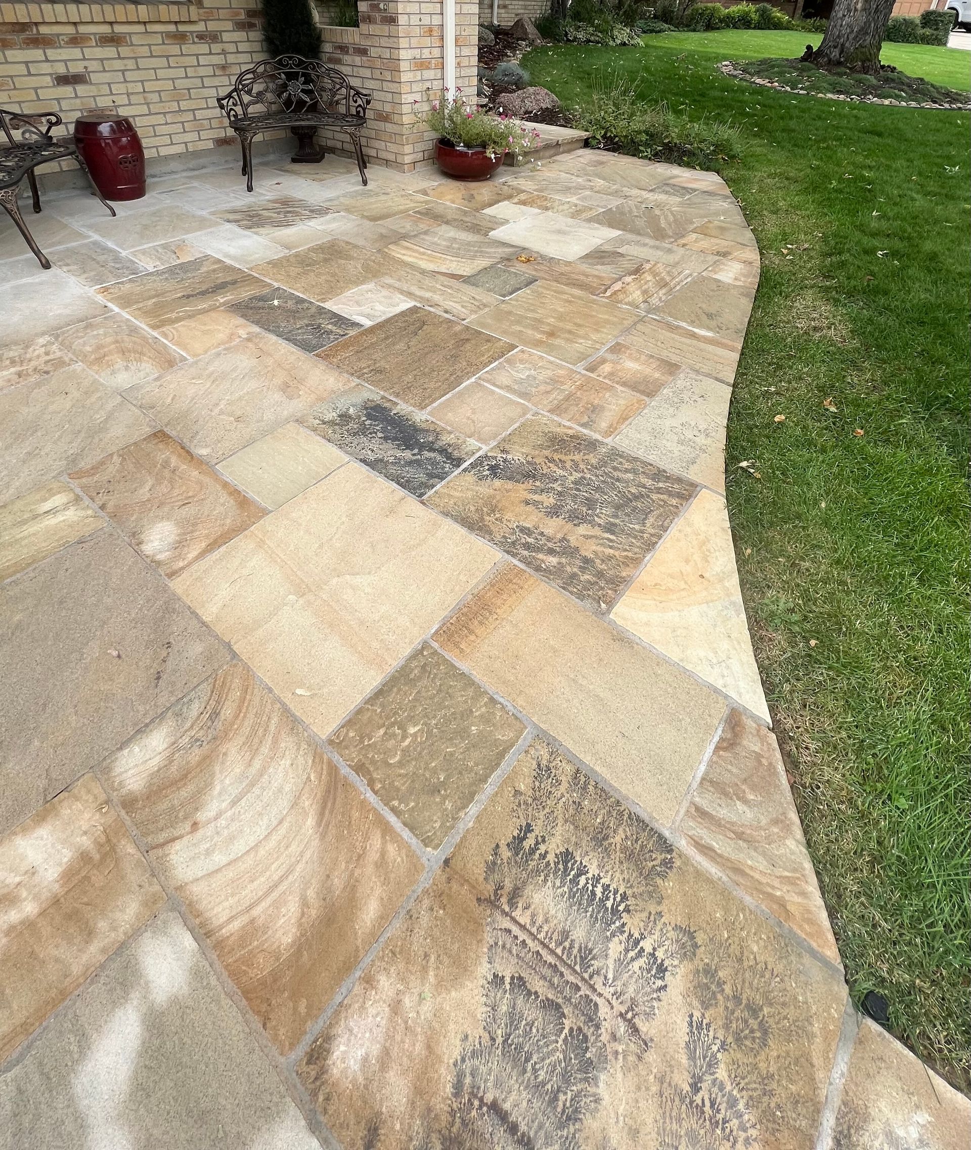 A stone patio with a brick wall and chairs in the background.