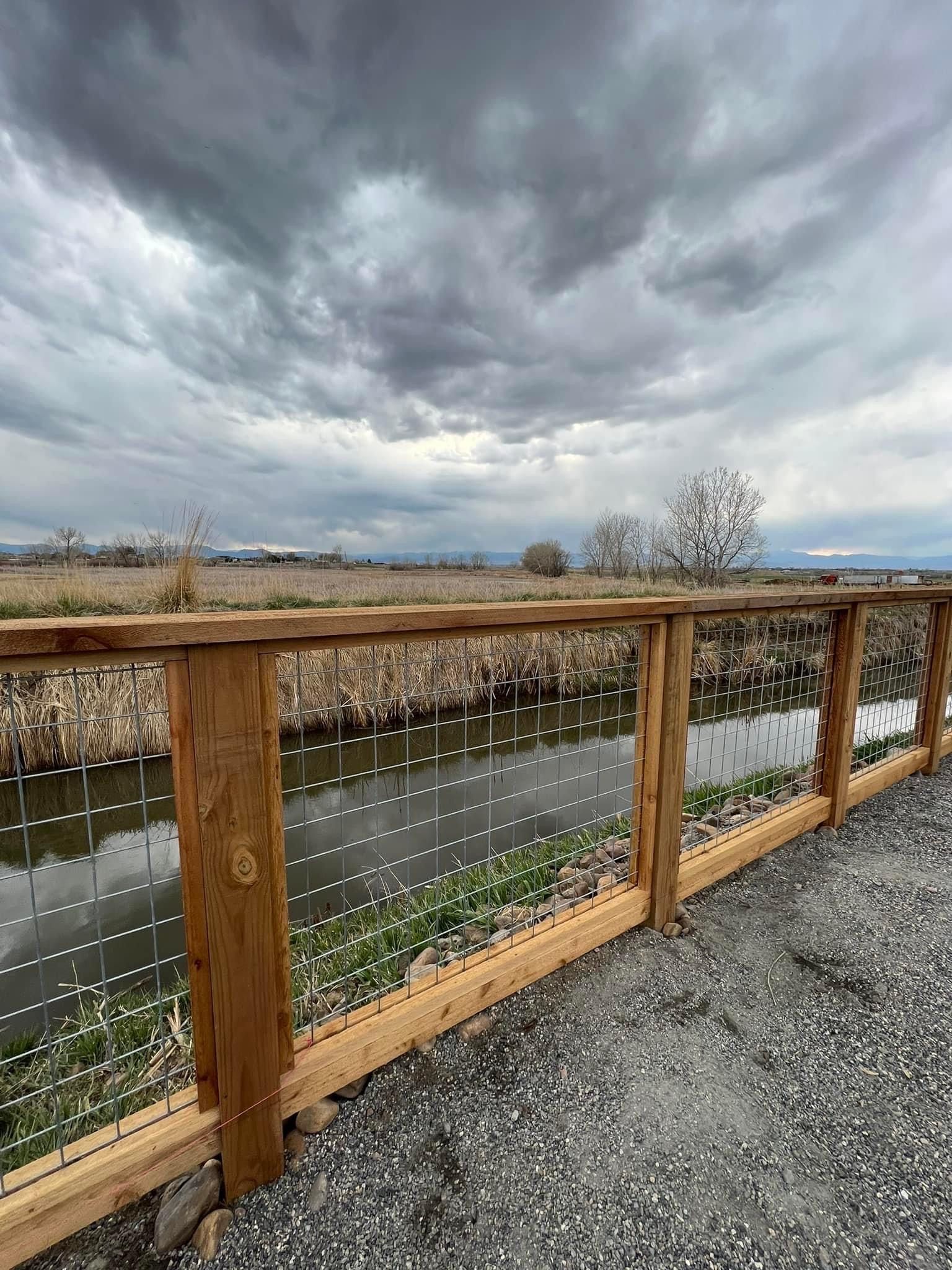A wooden fence surrounds a river with a cloudy sky in the background.