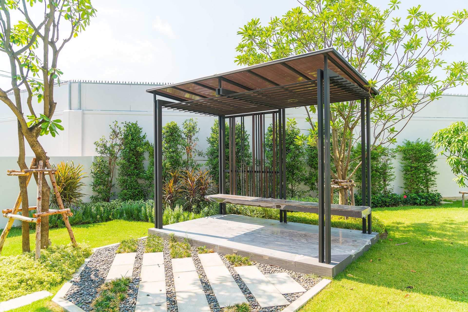 A wooden pergola with a paved seating area in a lush green garden.
