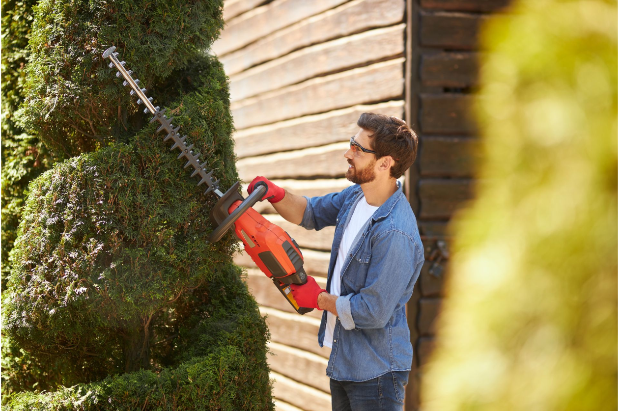 A man is cutting a bush with a hedge trimmer.
