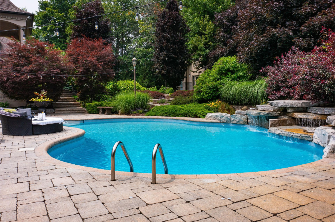 A large swimming pool with a waterfall in the backyard of a house.