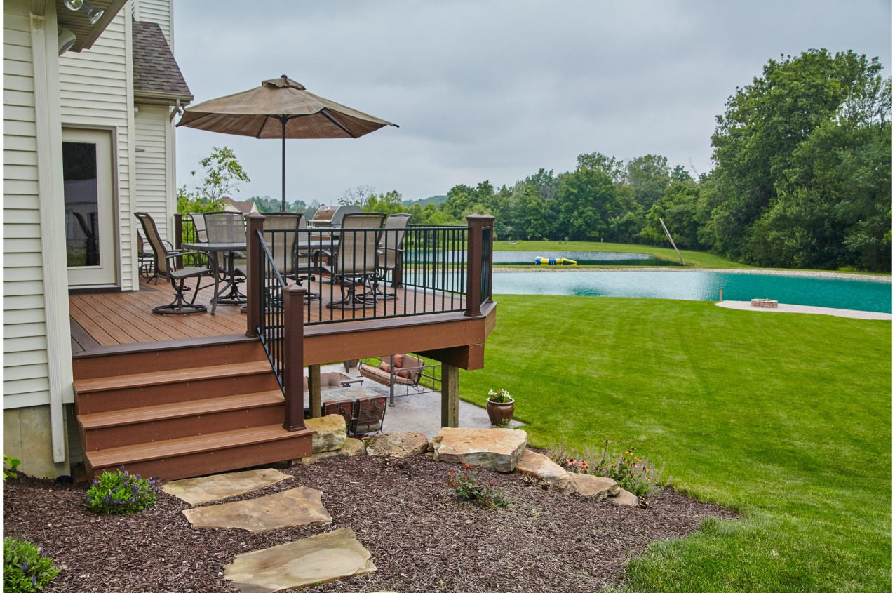 A deck with a table and chairs and an umbrella next to a swimming pool.