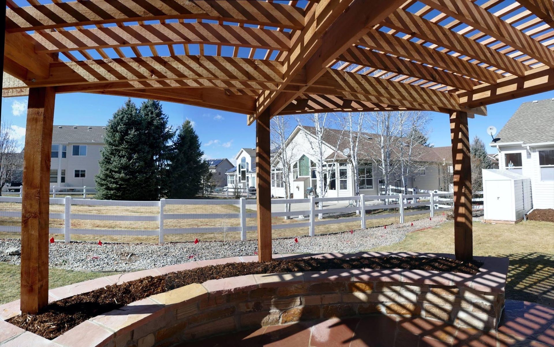 A wooden gazebo with a white picket fence in the background
