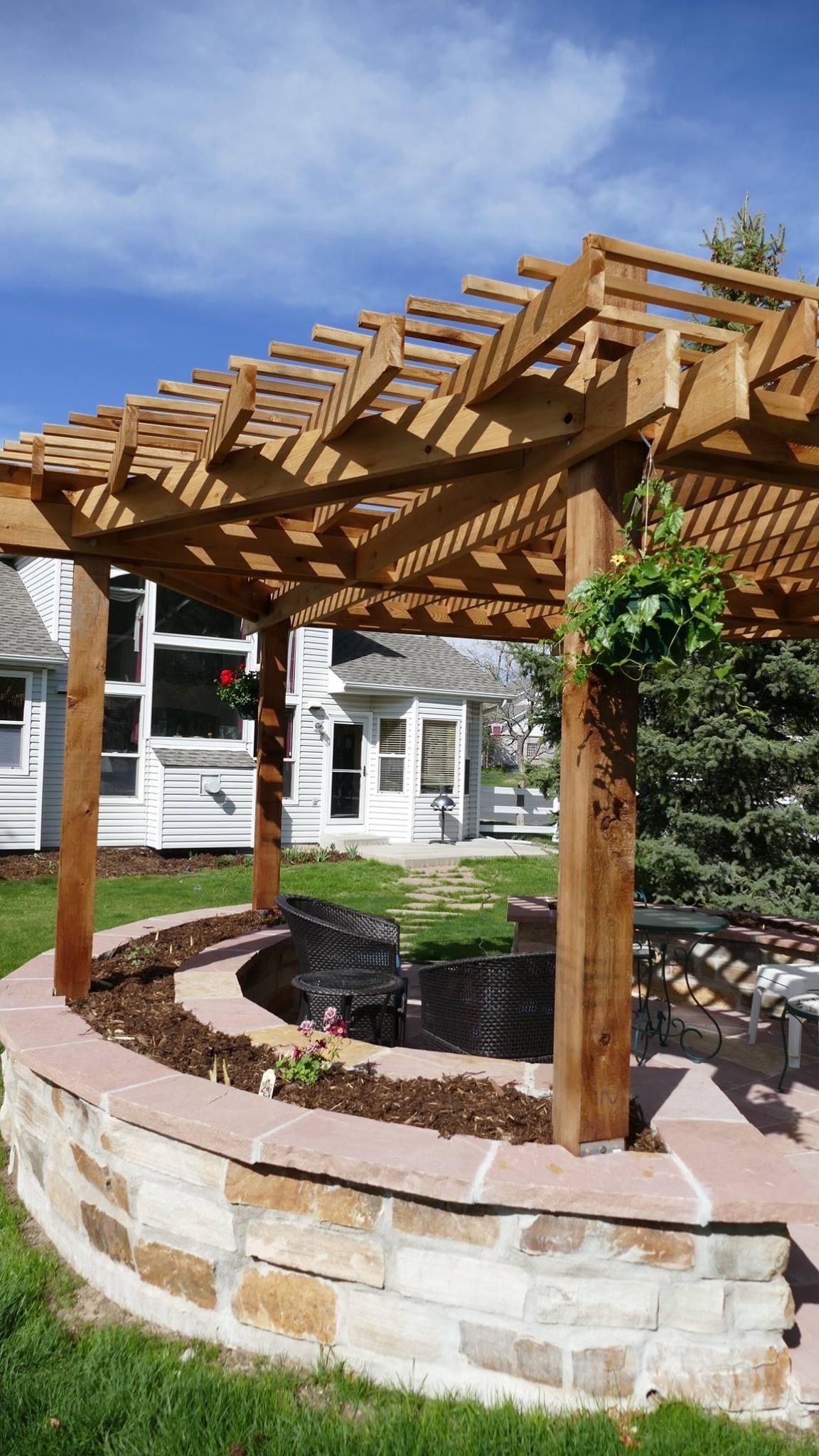 A wooden pergola is sitting on top of a stone wall in a backyard.