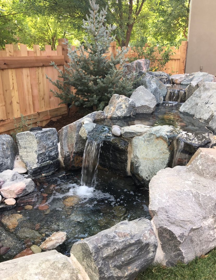 A waterfall in a backyard surrounded by rocks and a wooden fence.