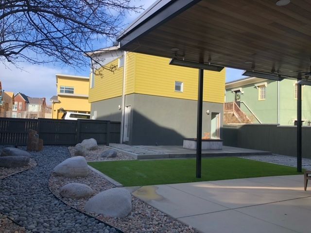 A backyard with a covered patio and a yellow house in the background