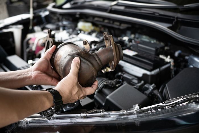 A person is holding a catalytic converter in front of a car engine.