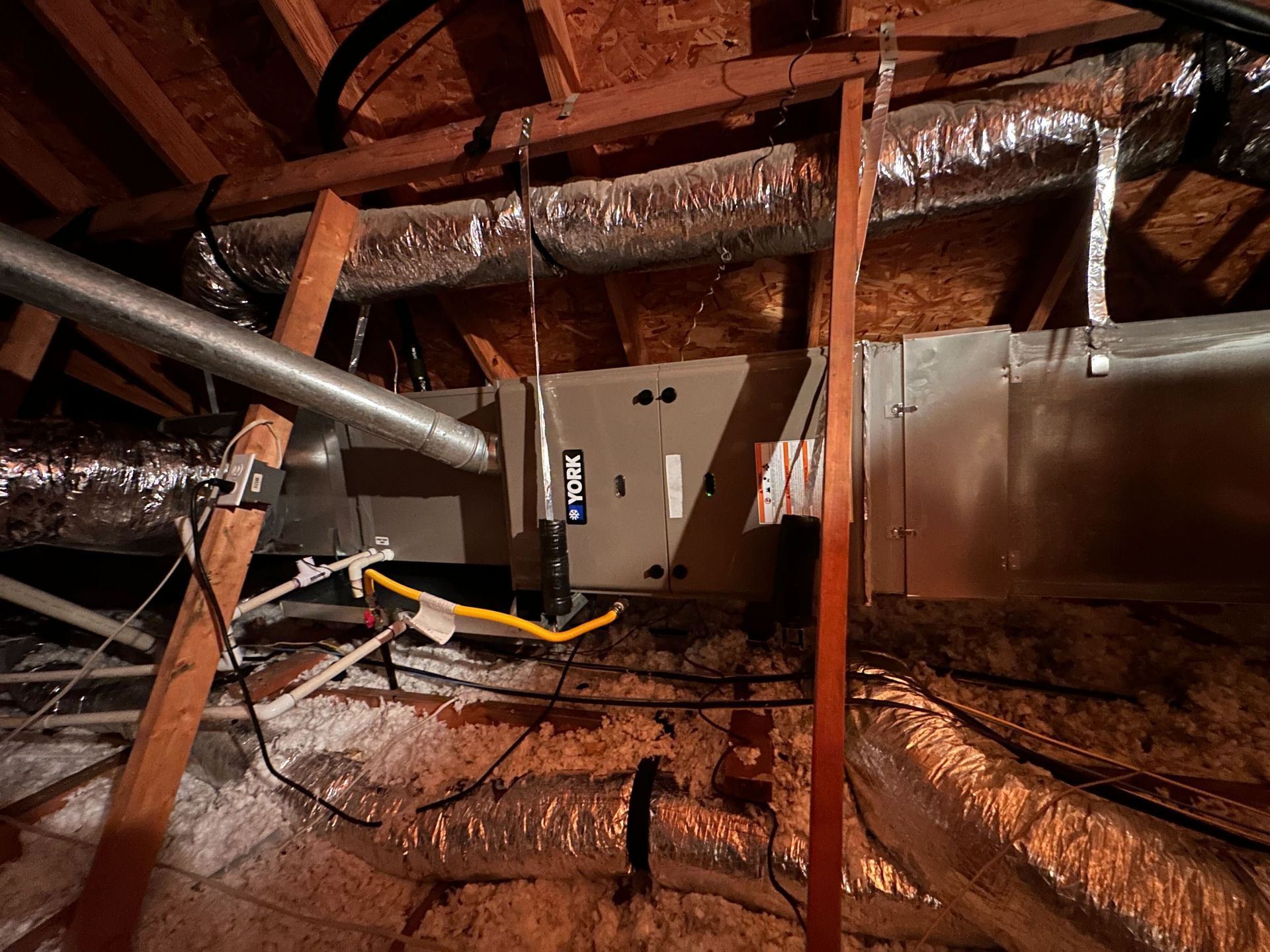 A ceiling with a lot of pipes and wires hanging from it.