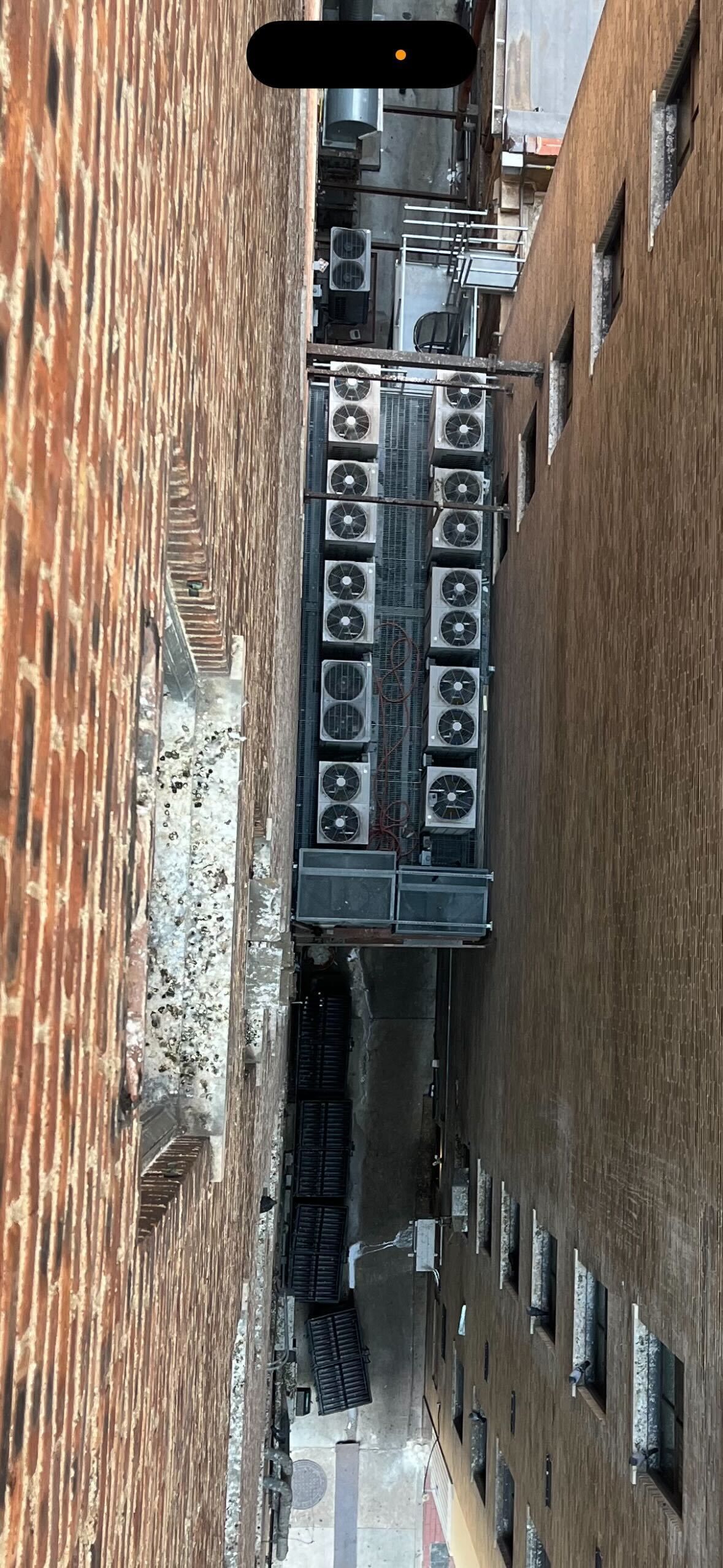 A narrow alleyway with a brick wall and a row of air conditioners on the side of a building.