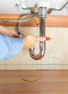 A person is fixing a sink pipe with a wrench.