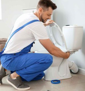 A man is kneeling down to fix a toilet in a bathroom.