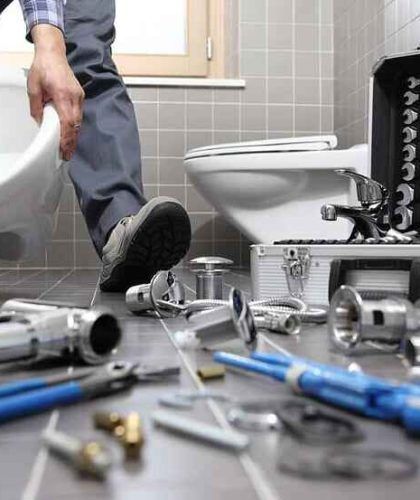 A plumber is fixing a toilet in a bathroom.