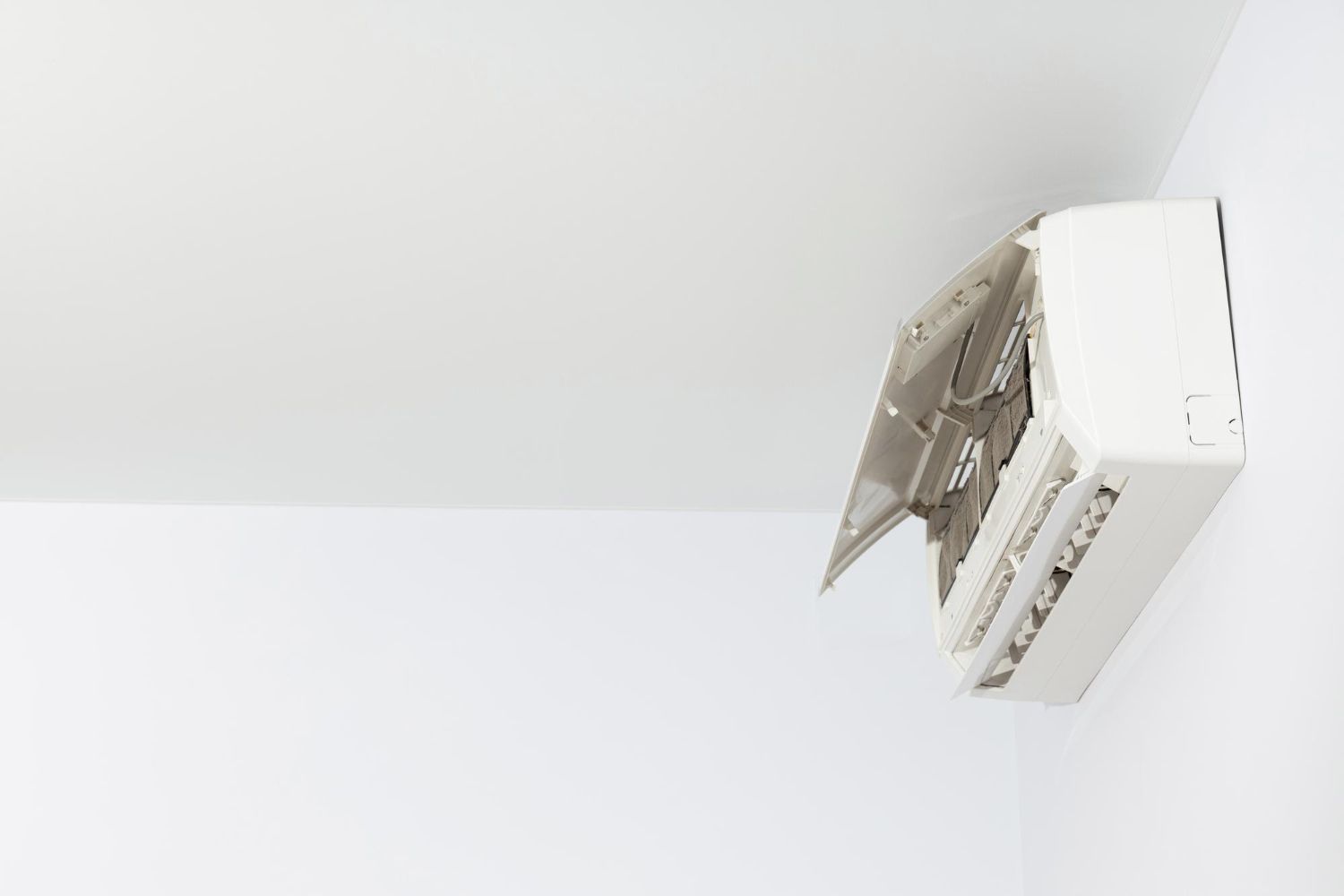 Open wall-mounted air conditioner with front panel and filter exposed on a white wall