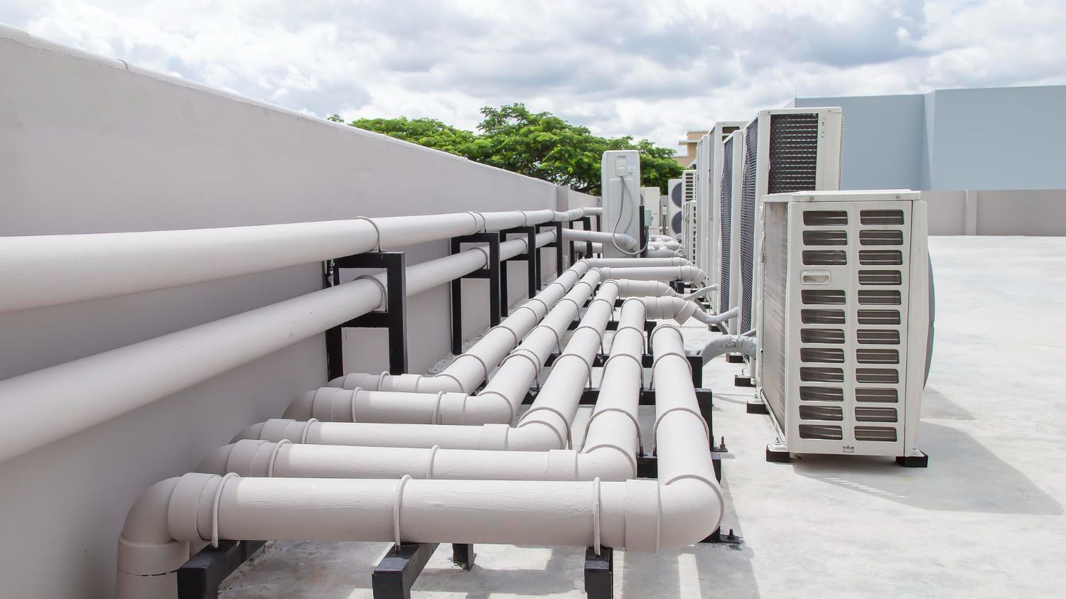 Rooftop with large white HVAC pipes and ducts running alongside air conditioning units