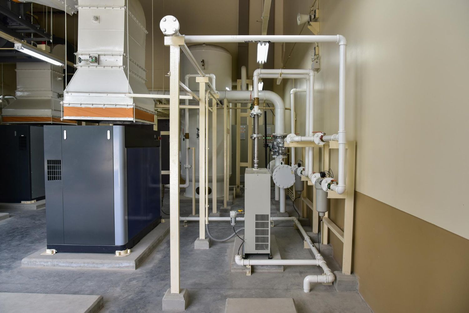 Industrial piping and machinery in a utility room with white pipes, valves, and a large metal unit