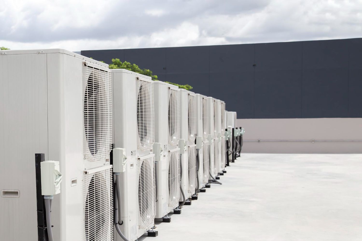 Row of white outdoor HVAC units on a rooftop under a cloudy sky