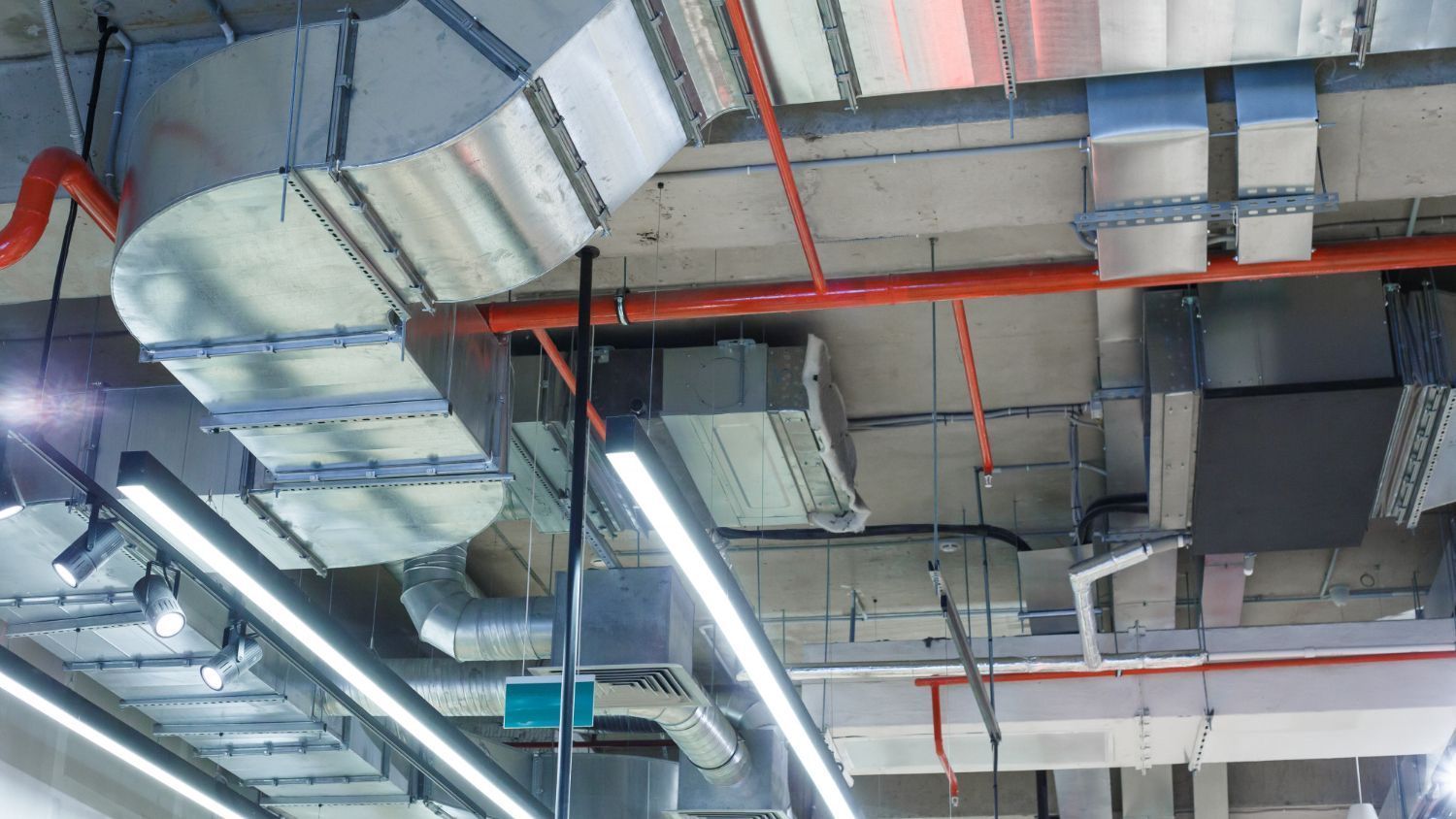 Industrial ceiling with exposed ducts, pipes, and fluorescent lights in a building interior