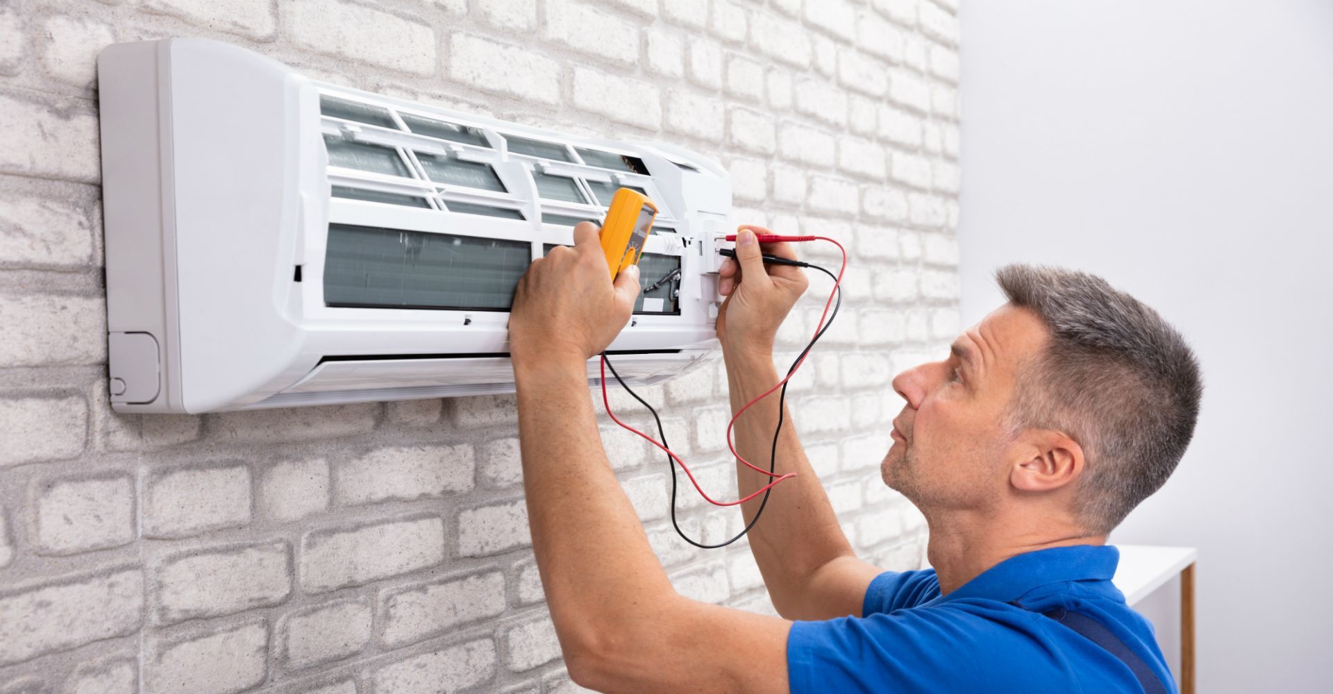Technician repairing a wall-mounted air conditioner with tools in a brick-walled room