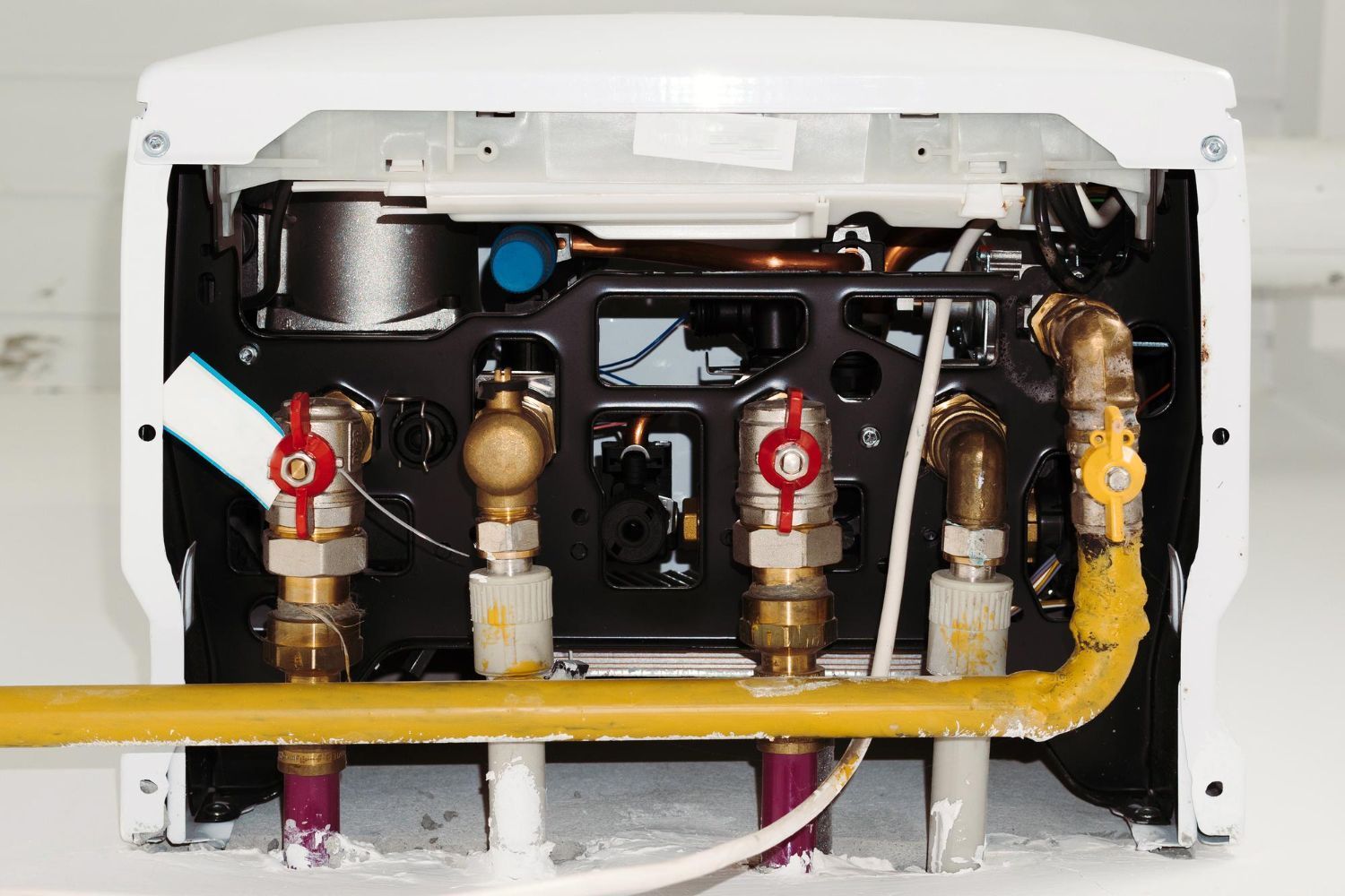 Open appliance interior with exposed pipes, valves, and yellow gas line under a white cover