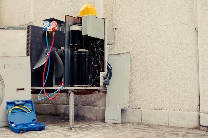 Outdoor utility equipment and exposed wiring beside a wall, with a blue toolbox on the ground.