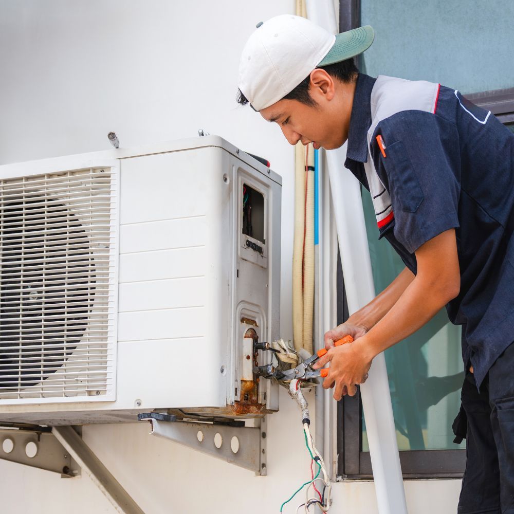 Technician in hard hat repairing an outdoor air conditioner unit attached to a building wall