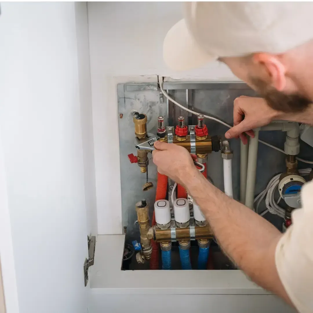 Plumber adjusting valves on a wall-mounted heating manifold inside a utility cabinet.