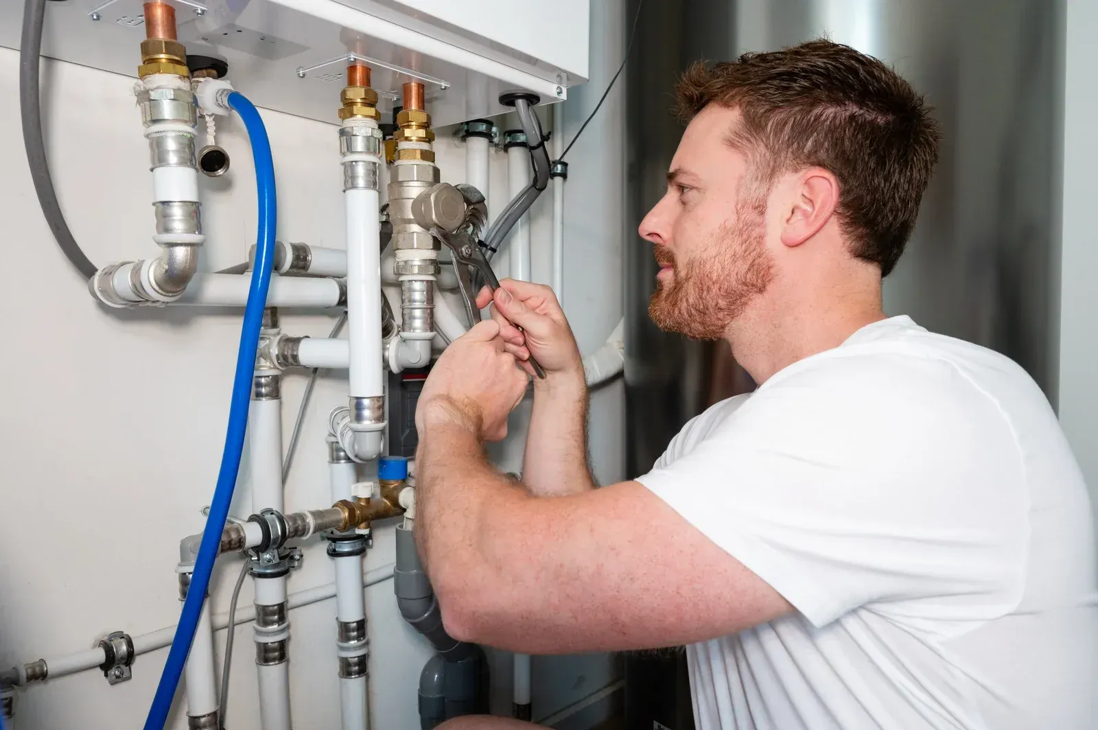 Technician inspecting pipes and valves in a utility room, using a wrench